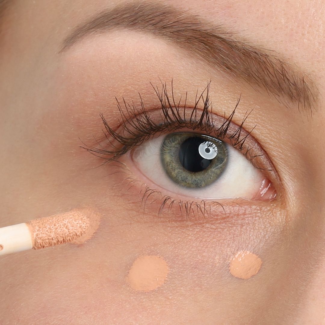 Applikator mit Concealer-Textur unter dem Auge aufgetragen.