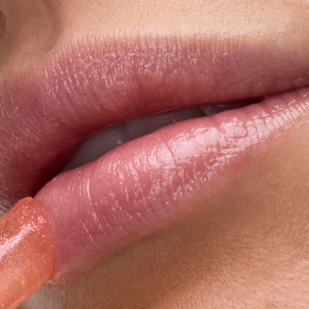 Nahaufnahme von Lippen. Der Lip Balm wird aufgetragen. Rosa getönter Lip Balm. Glänzendes Finish.