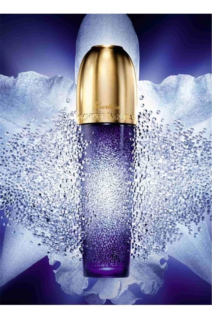 Blau-violette Flasche mit goldfarbenem Deckel. Aufschrift: Guerlain Orchidée Impériale. Umgeben von weißen Perlen.