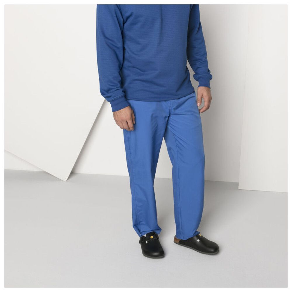Person trägt schwarze Pantoletten. Blaue Hose und Oberteil. Schuhe mit gelbem Logo.