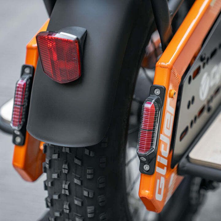 Rücklicht und Kotflügel eines orangefarbenen Fahrrads. Zwei rote Rücklichter und schwarzer Kotflügel.