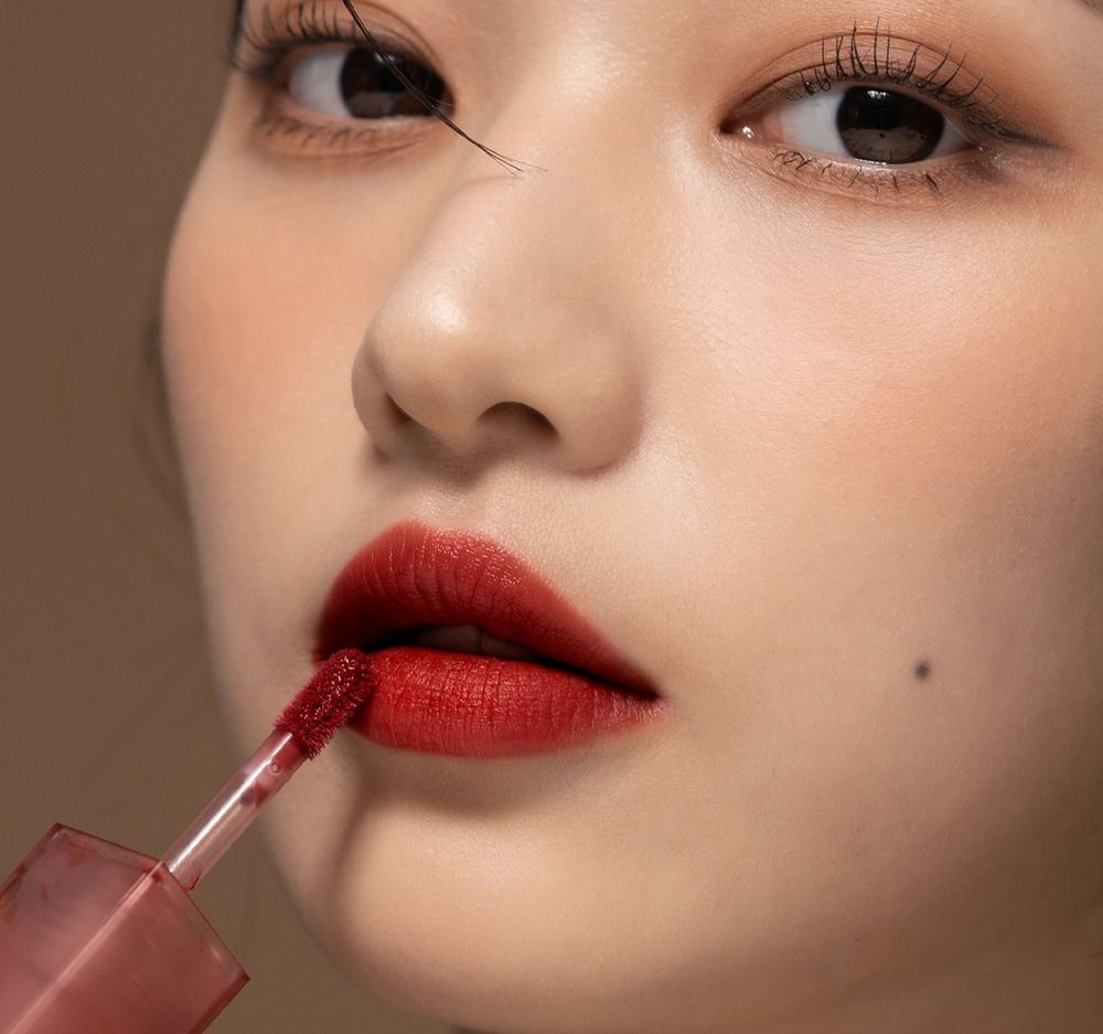 Nahaufnahme einer Frau, die Lipgloss aufträgt. Rote Lippen. Applikator sichtbar. Hautton.