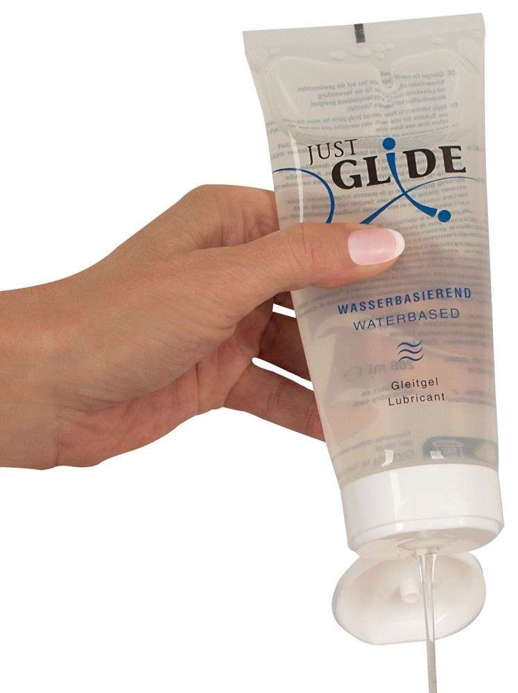 Hand hält Tube, Gel fließt heraus. Aufschrift: JUST GLIDE, wasserbasiert, Gleitgel.