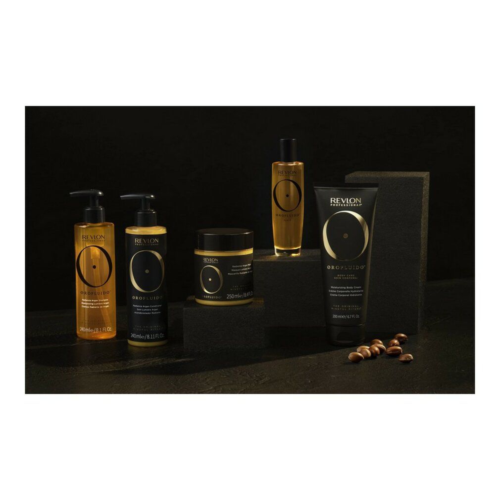 Orofluido-Produkte auf schwarzem Hintergrund. Flaschen, Tiegel und Tube in Gold und Schwarz. Argan-Samen liegen daneben.