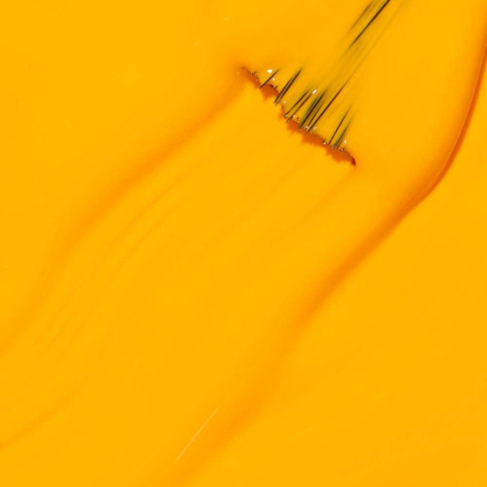 Gelber Nagellack-Pinselstrich. Die Borsten sind sichtbar. Der Lack ist glänzend.