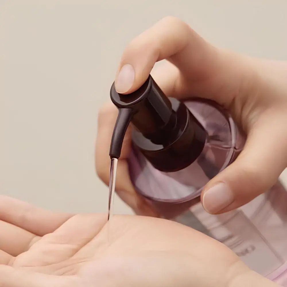 Hände drücken Produkt aus einer Flasche mit Pumpe. Flüssigkeit fließt in die Handfläche.