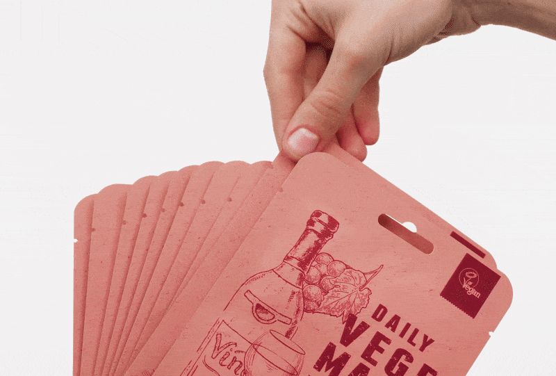 Hand hält mehrere rosa Maskenverpackungen. Aufdruck: DAILY VEGE MASK, Wein-Illustration. Verpackungen mit Aufhängeloch.