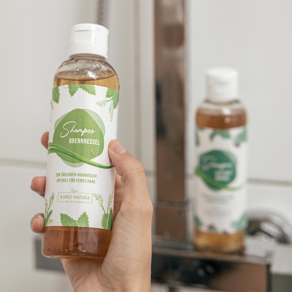 Person hält Shampoo-Flasche. Im Hintergrund eine weitere Flasche und ein Wasserhahn.