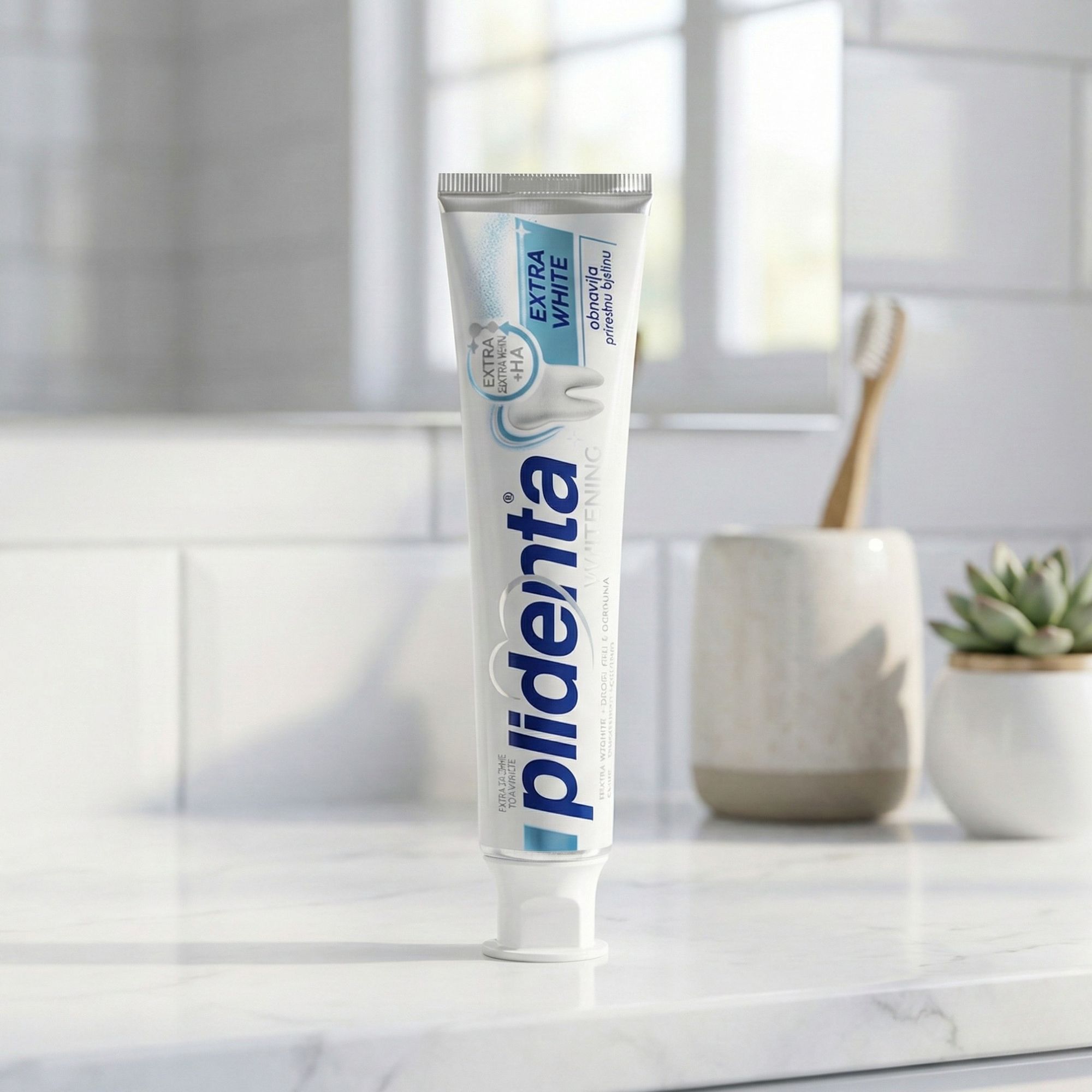 Zahnpasta-Tube auf einer weißen Oberfläche. Im Hintergrund: Waschbecken, Zahnbürste. Aufschrift: plidenta, EXTRA WHITE. Enthält HA.