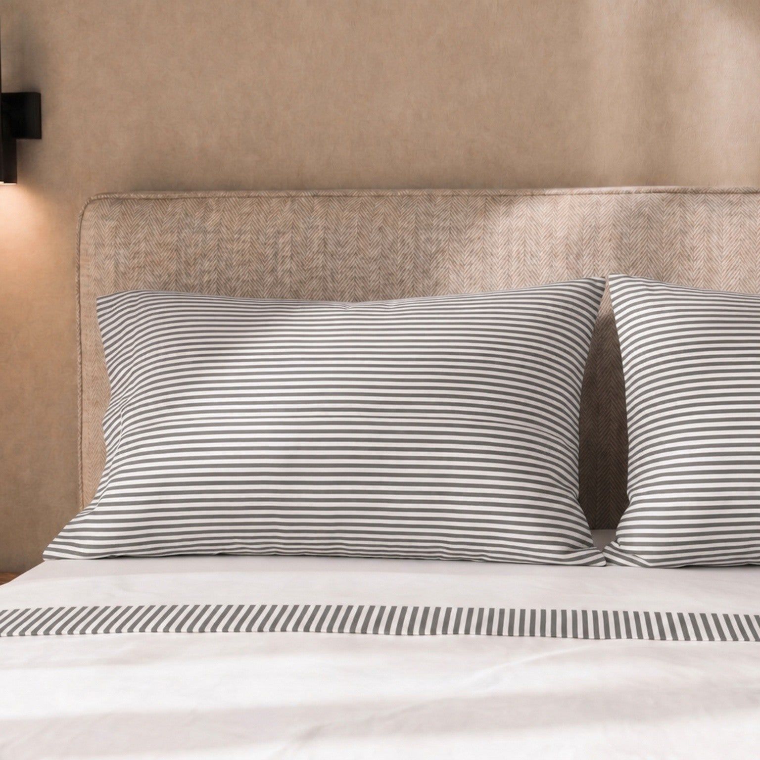Kissenbezüge und Bettlaken mit dezentem Streifenmuster auf einem Bett.
