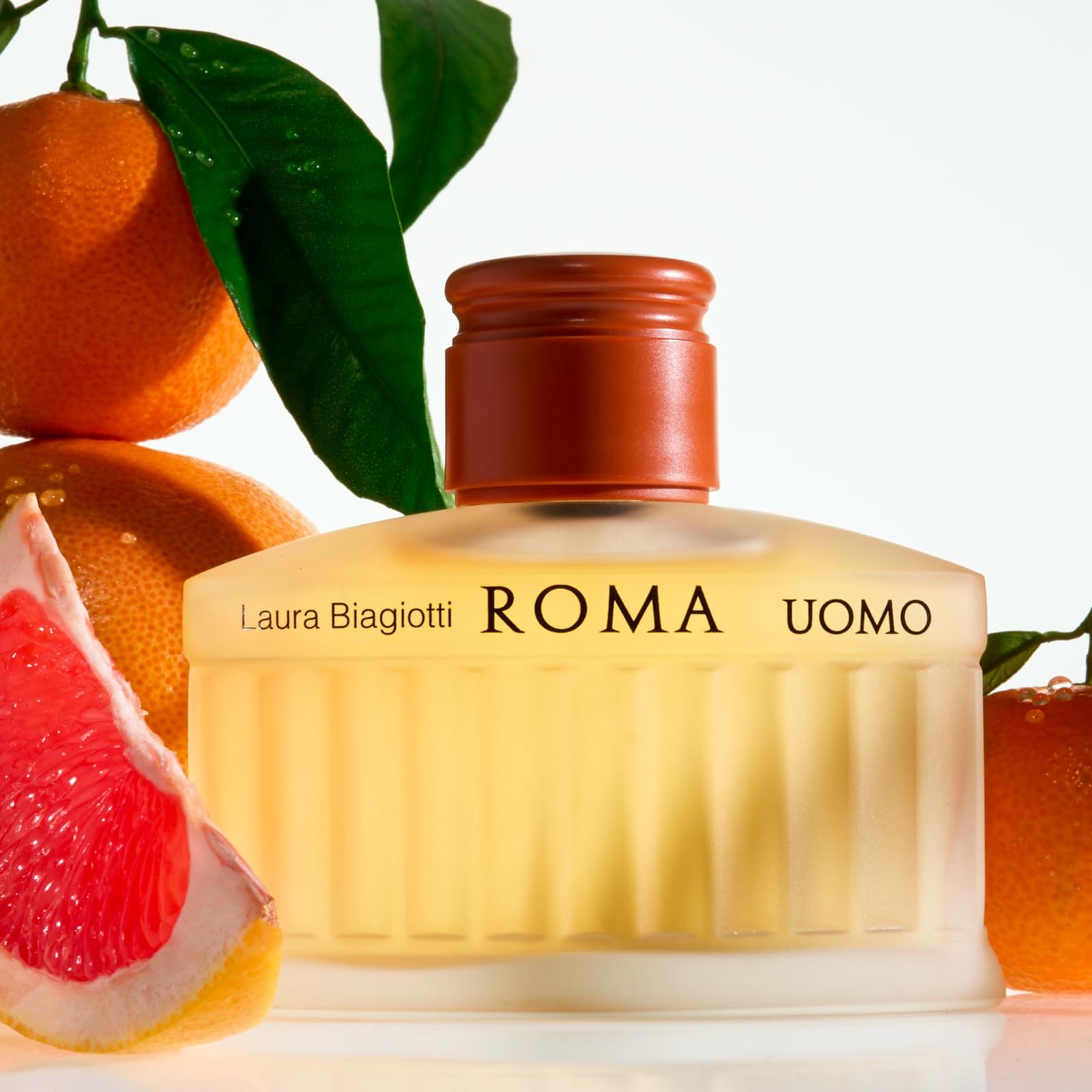 Parfümflakon mit gelblicher Flüssigkeit. Aufschrift: Laura Biagiotti ROMA UOMO. Umgeben von Orangen und Grapefruit.