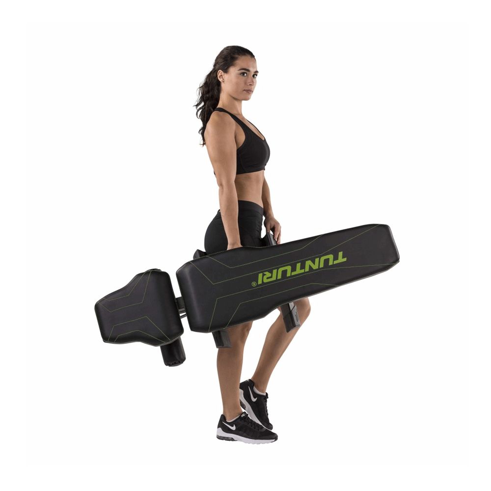 Frau trägt zusammengeklappte Flachbank. Schwarze Bank mit grünen Akzenten. Aufschrift TUNTURI.