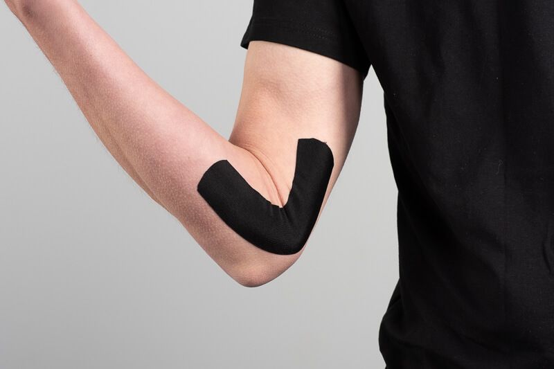 Schwarzes Kinesiotape am Ellenbogen einer Person. Tape in V-Form angebracht. Hautfarbe sichtbar.