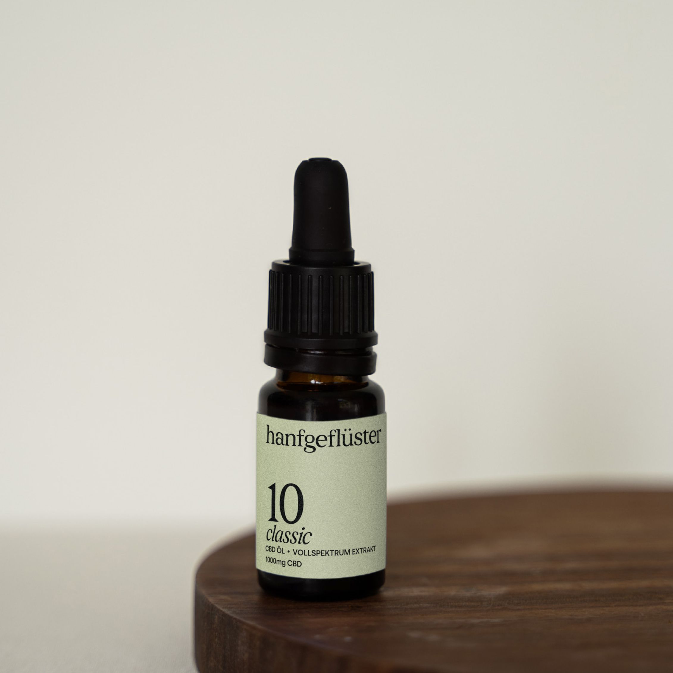 Braune Glasflasche mit schwarzem Tropfer auf Holzbrett. Aufschrift: hanfgeflüster 10 classic. Vollspektrum Extrakt. 1000mg CBD.