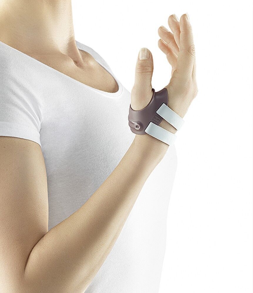 Person trägt Daumenorthese. Graue Schale, weiße Riemen. Handgelenk und Daumen umschließend. Arm vor weißem Hintergrund.