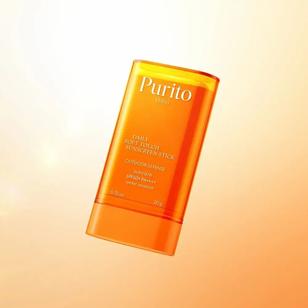 Schwebender, orangefarbener Sonnenschutz-Stick. Text: Purito, Daily Soft Touch Sunscreen Stick, SPF50+ PA++++, 0.70 oz, 20 g.