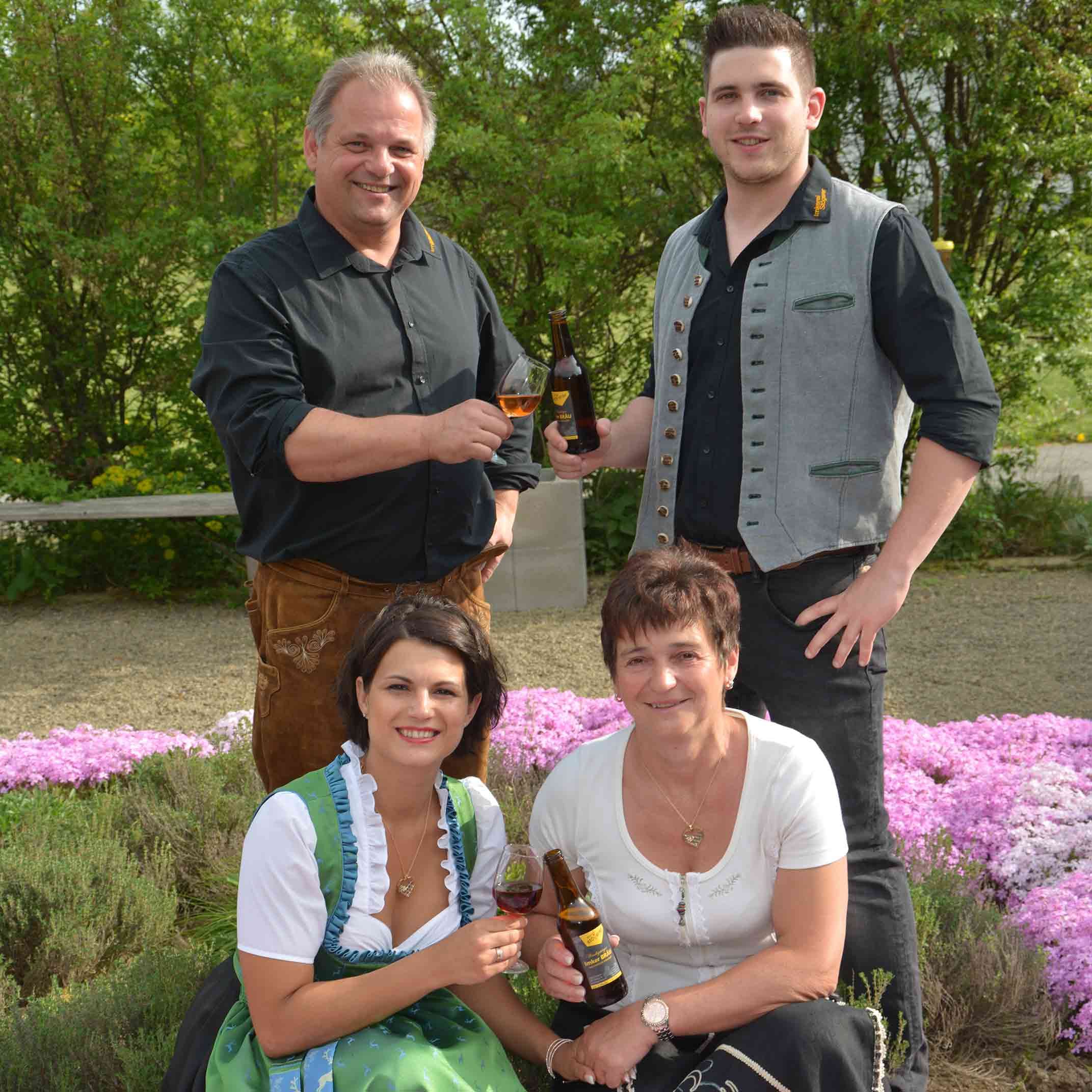 Vier Personen in Tracht mit Bierflaschen und Gläsern im Freien.