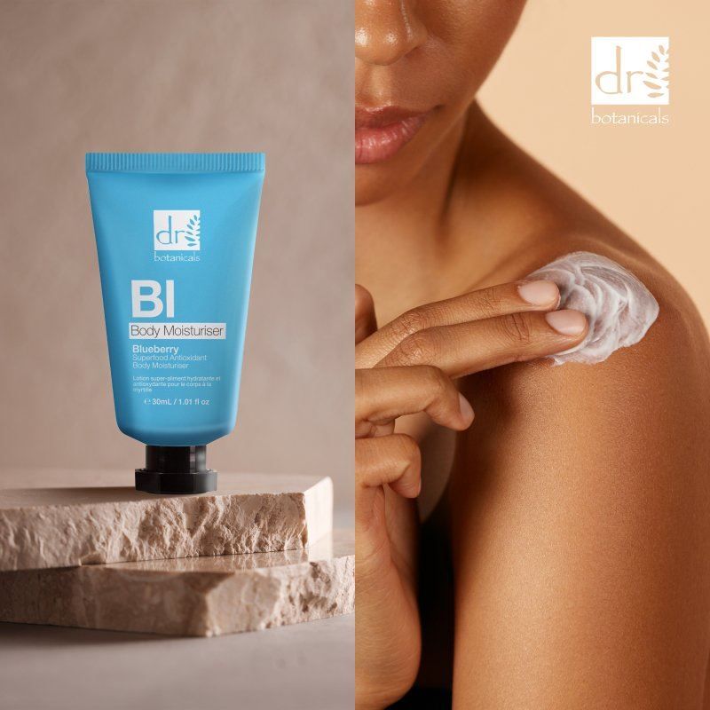 Dr. Botanicals Blaubeer-Körperlotion neben einer Schulter, auf die Creme aufgetragen wird.