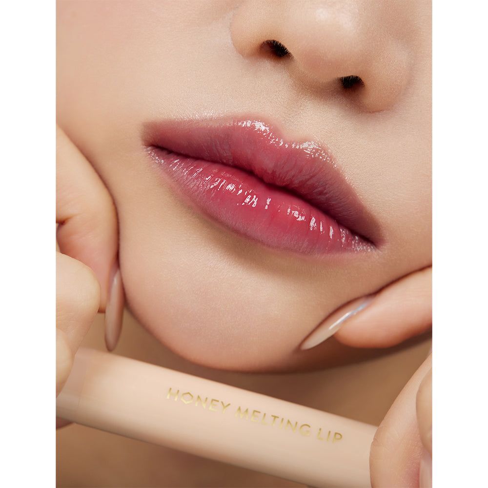 Nahaufnahme von Lippen mit glänzendem Lippenstift. Ein Lippenstift mit der Aufschrift 'HONEY MELTING LIP' wird gehalten.