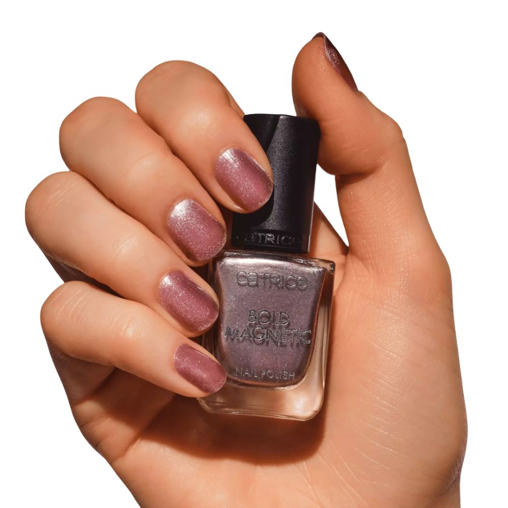 Hand hält Nagellackflasche Catrice Bold Magnetic. Lackierte Nägel. Rosa-goldener Lack.