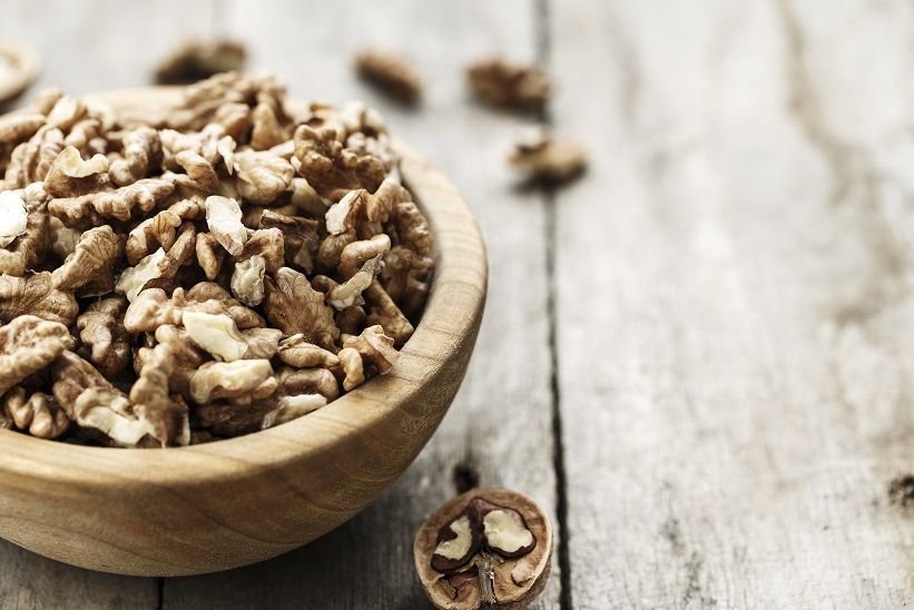Holzschale mit Walnusskernen auf Holzoberfläche. Einige Kerne verstreut.