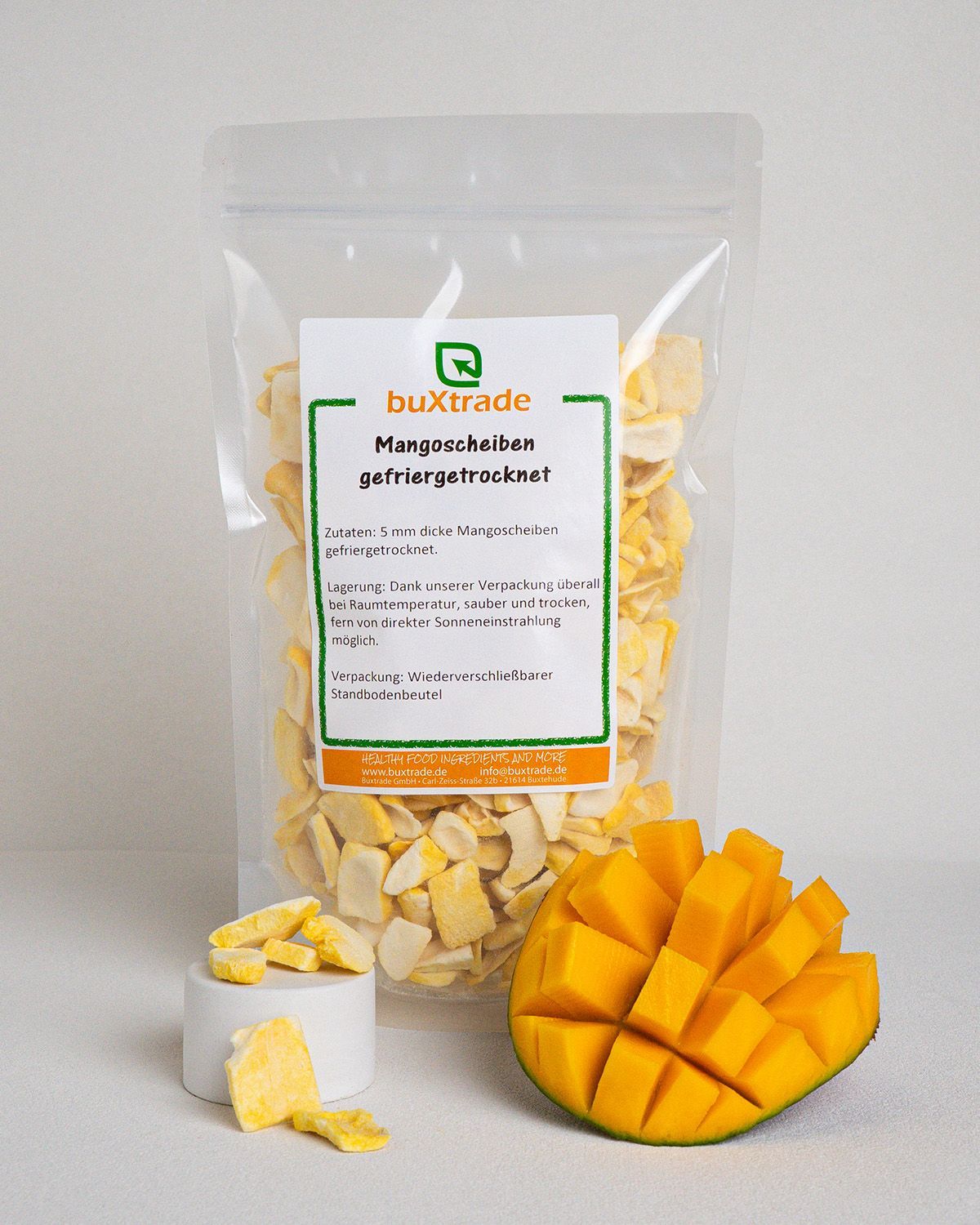 Transparente Verpackung mit Mangoscheiben, daneben eine Mango-Hälfte. Auf dem Etikett steht 'buXtrade'.