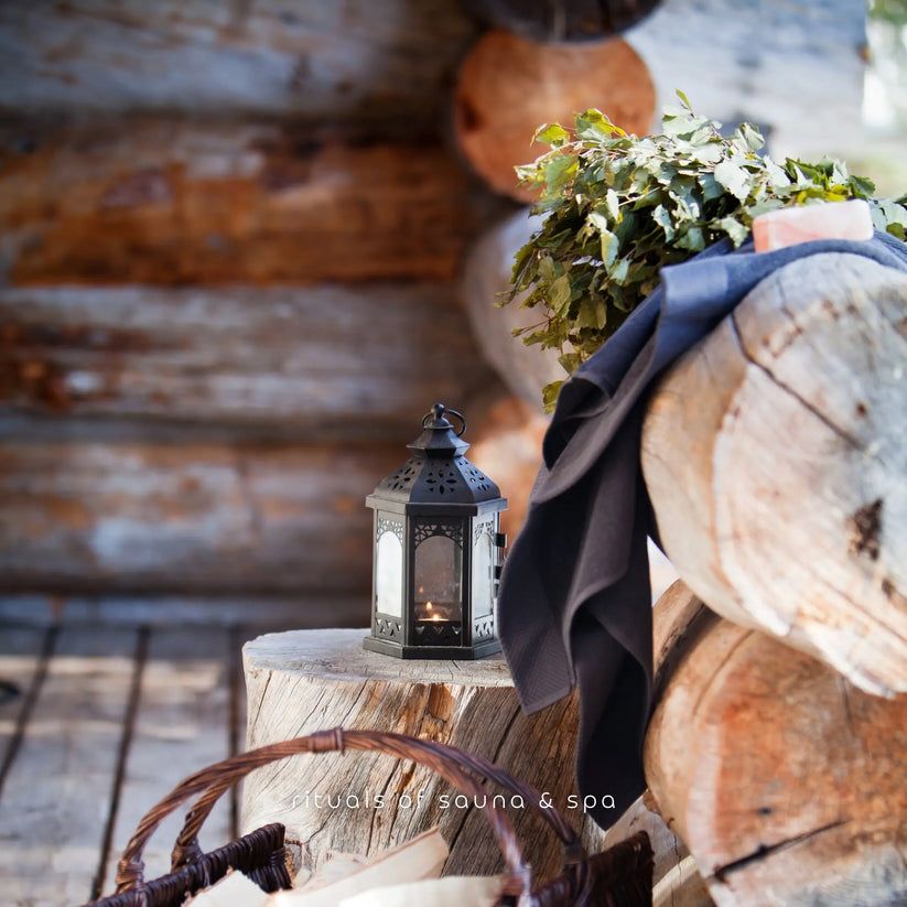 Holzstamm mit Laterne, Blättern und Korb. Im Hintergrund Sauna-Elemente.