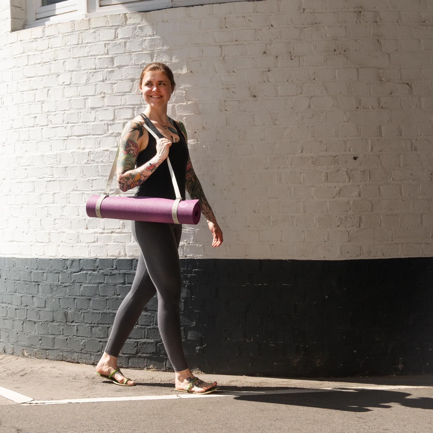 Person trägt eine Yogamatte mit Tragegurt. Die Matte ist lila. Die Person trägt Sportkleidung.