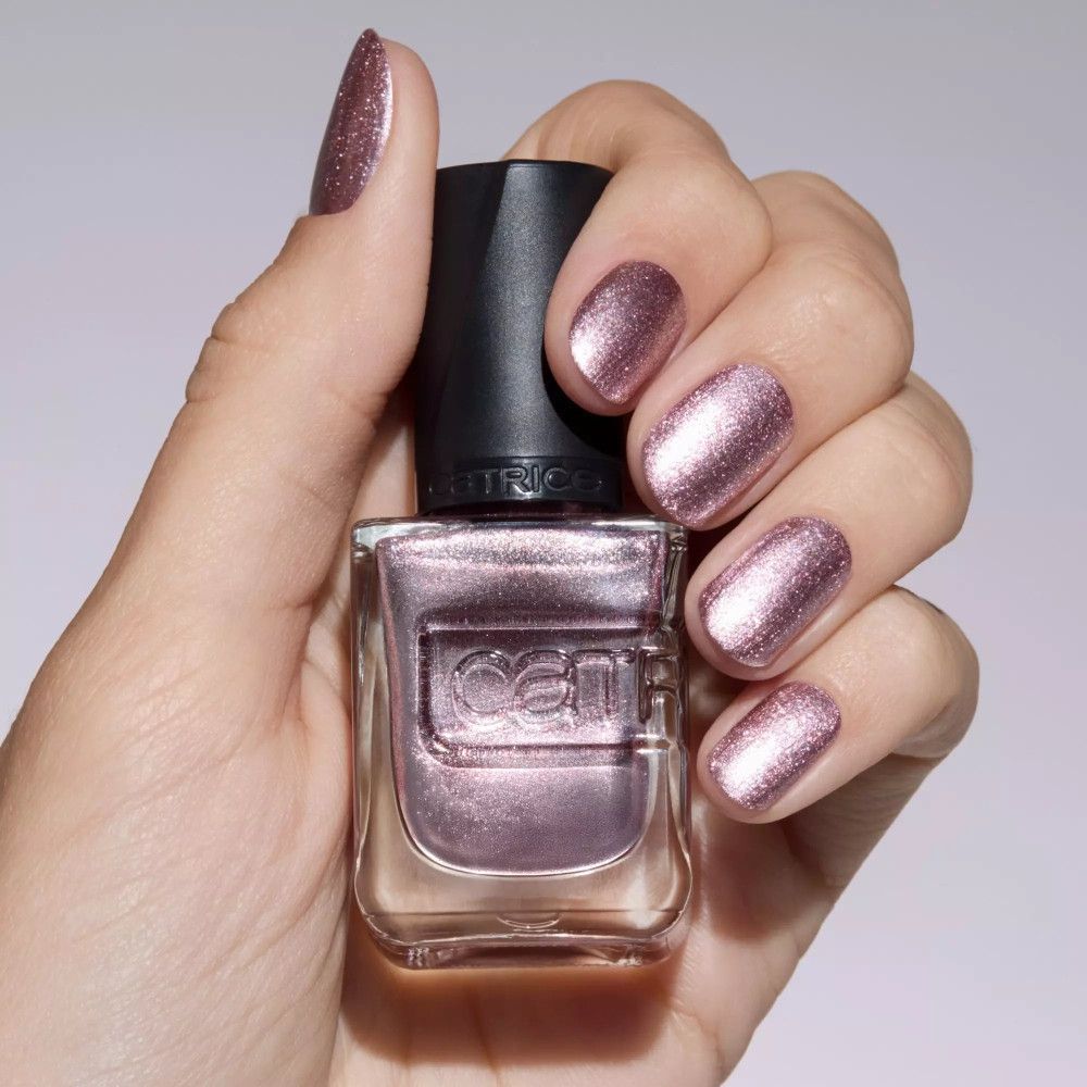 Hand mit lackierten Nägeln und Nagellackflasche. Der Lack ist rosa-metallic. Der Markenname ist sichtbar.