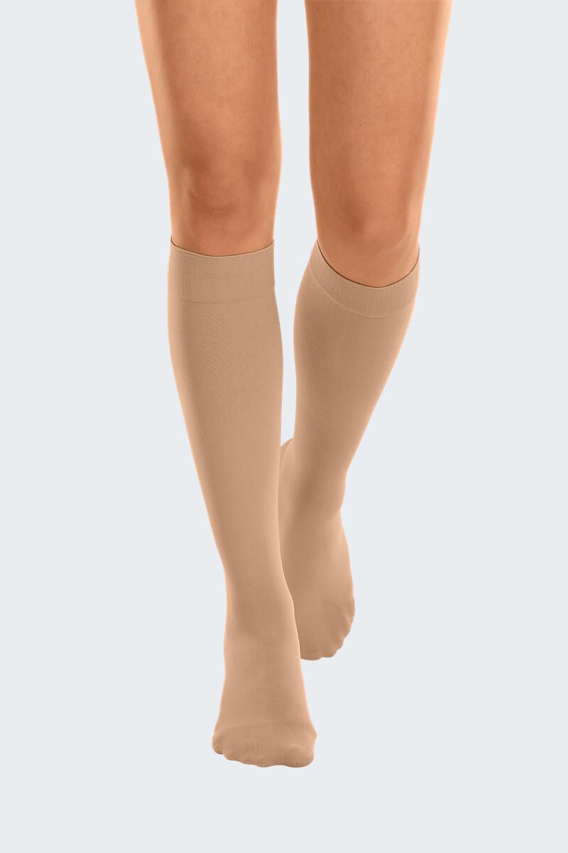 Hautfarbene Kompressionsstrümpfe, knielang, an Beinen einer Person. Blick von vorne.