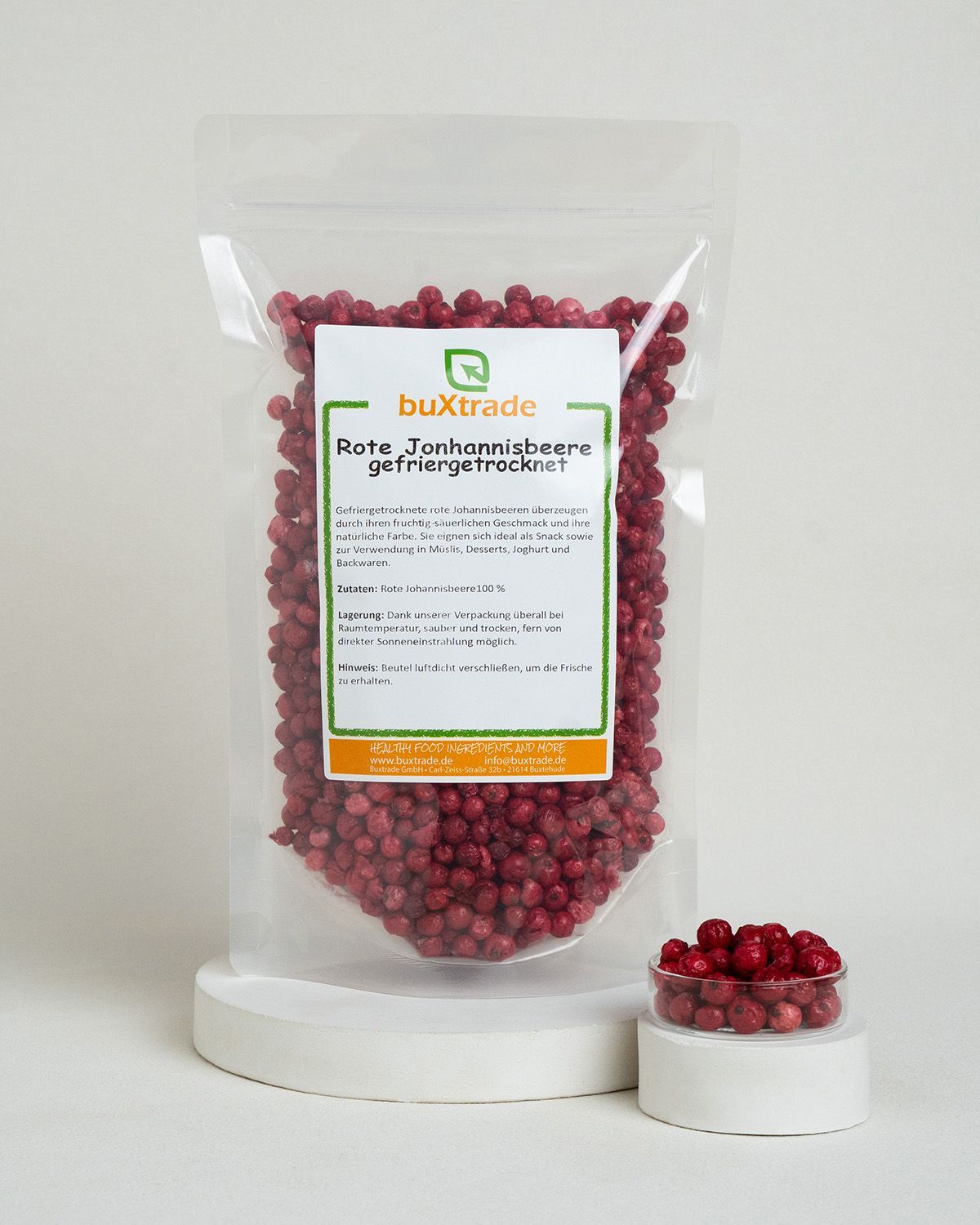 Gefriergetrocknete rote Johannisbeeren in Beutel und Schale, auf weißem Podest.