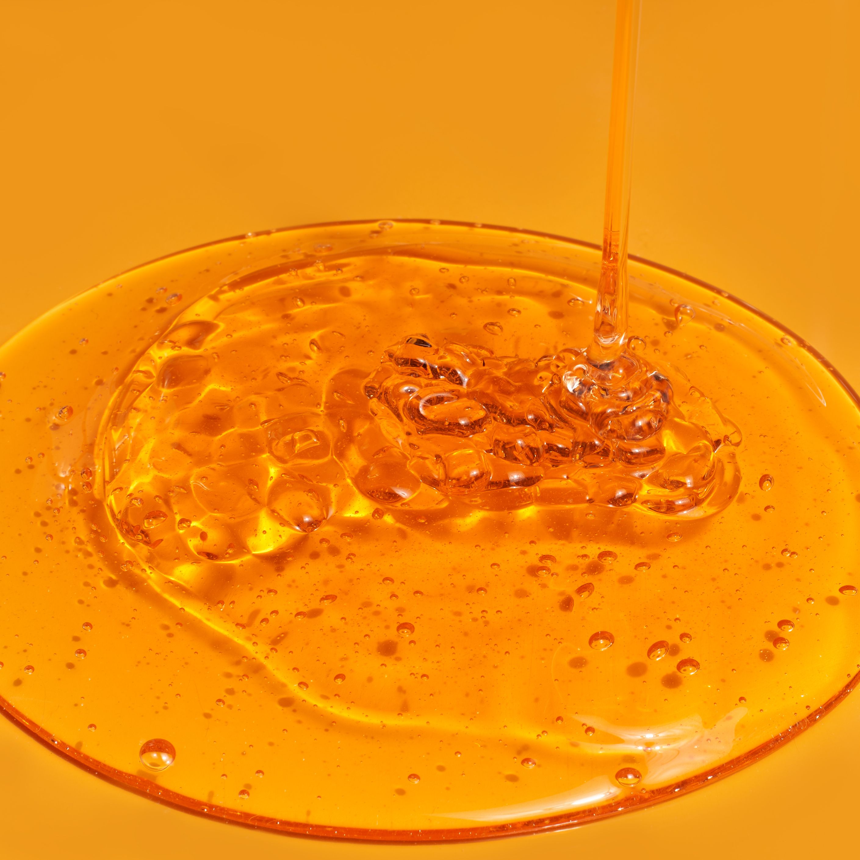 Flüssigkeit, die auf einer Oberfläche verteilt wird. Die Flüssigkeit ist bernsteinfarben und hat Blasen.