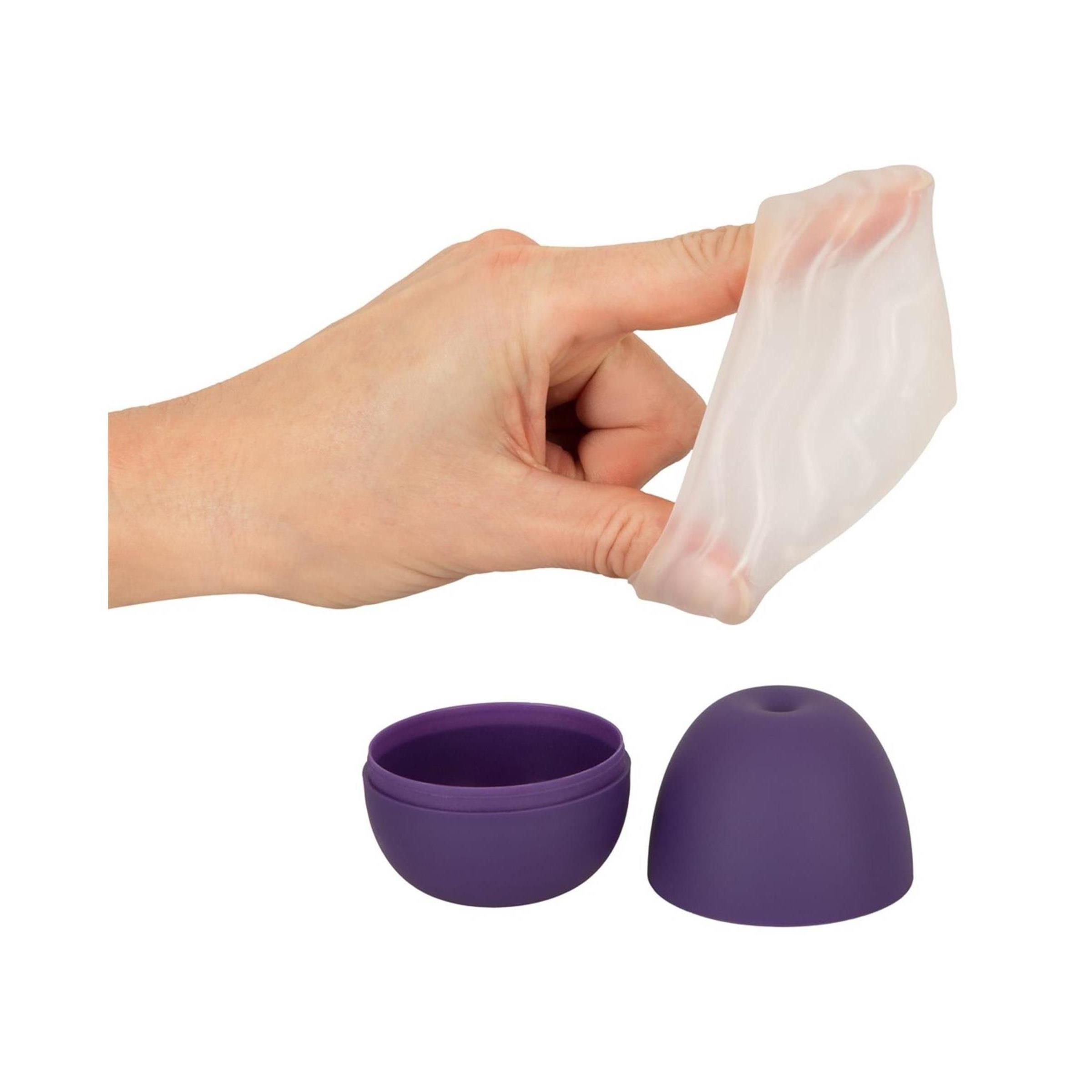 Hand hält ein dünnes, weißes, flexibles Material über einem geöffneten lila Eiform-Behälter.