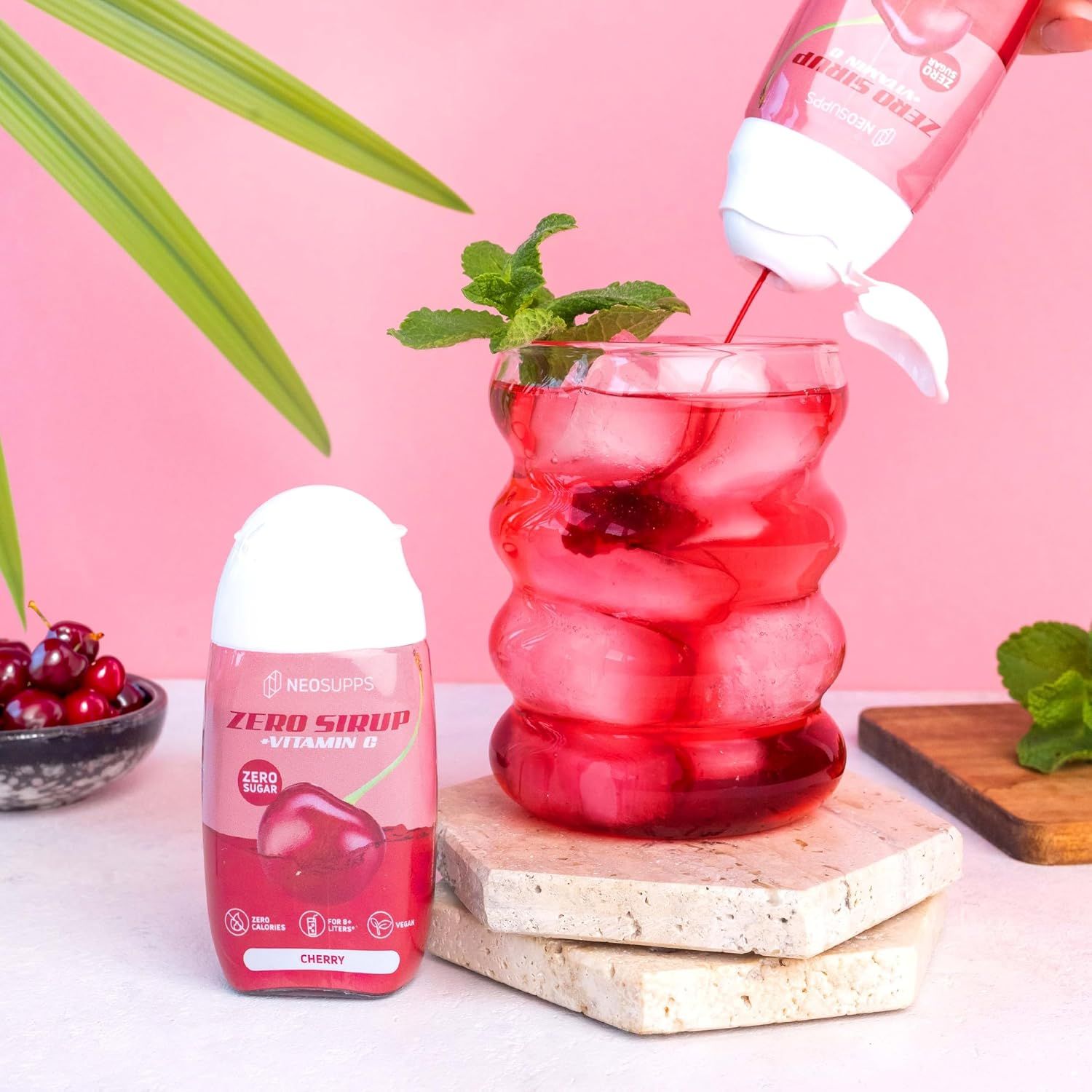 Sirup wird in ein Glas mit Eis gegossen. Aufschrift: Neosupps Zero Sirup, Cherry, Vitamin C. Kirschen und Minze als Dekoration.