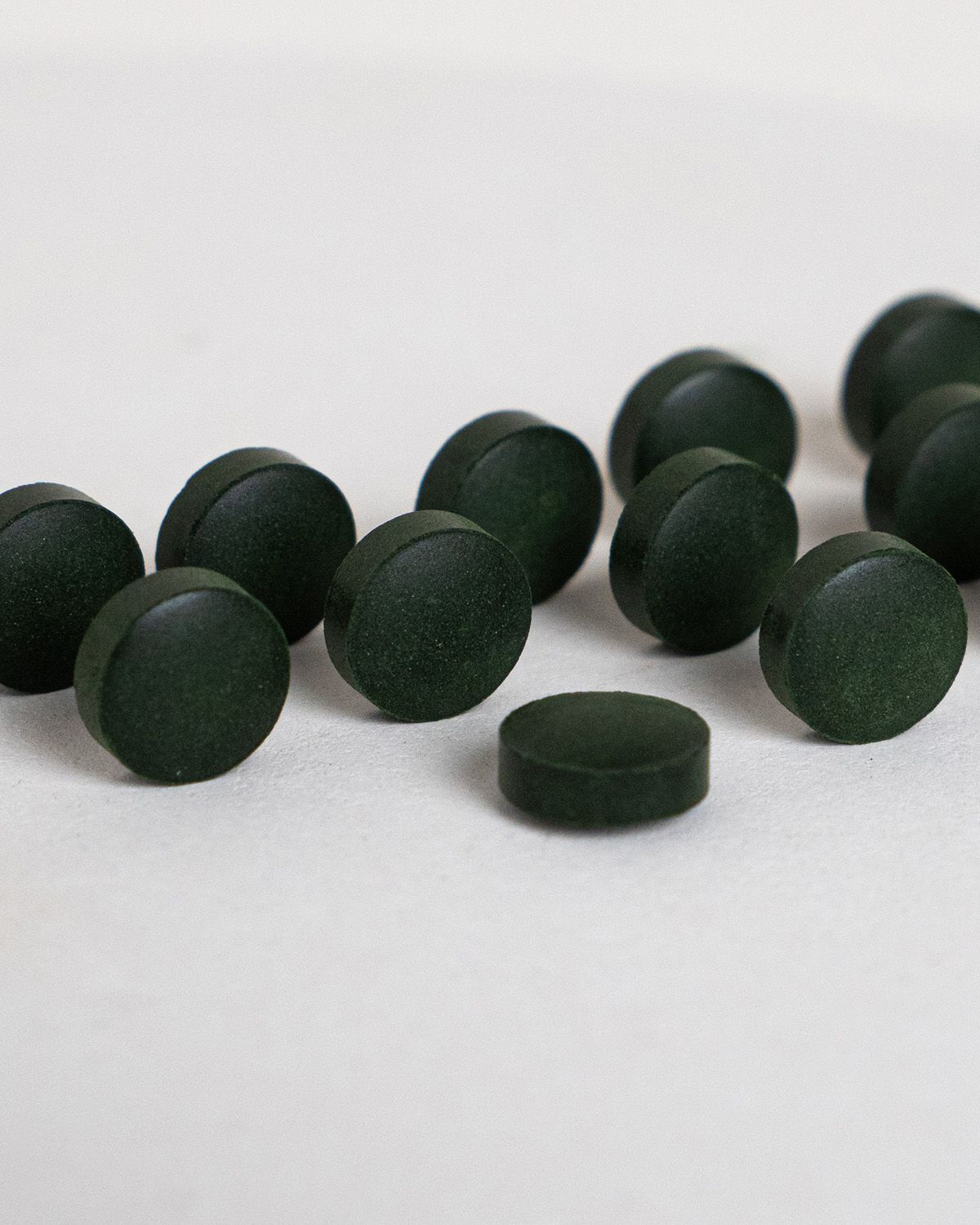 Dunkelgrüne, runde Tabletten auf weißem Untergrund. Einige Tabletten liegen verstreut.