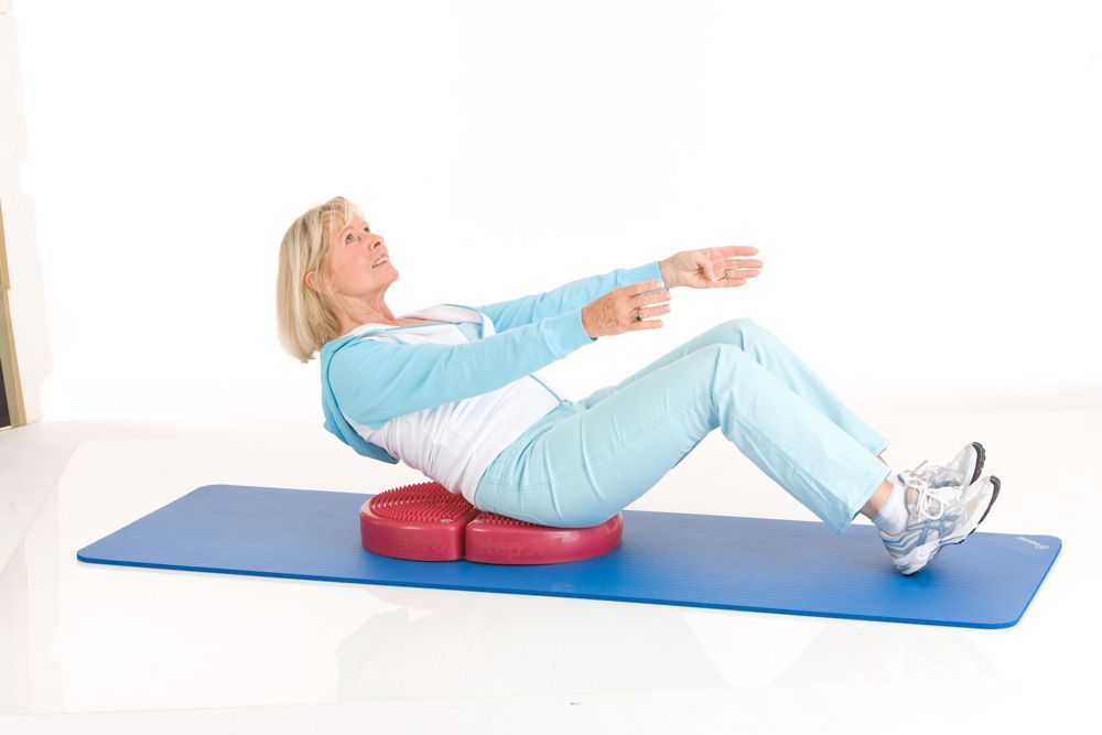 Frau auf rotem TOGU Aero Step XL® auf blauer Matte. Sie macht Bauchmuskeltraining. Weißer Hintergrund.