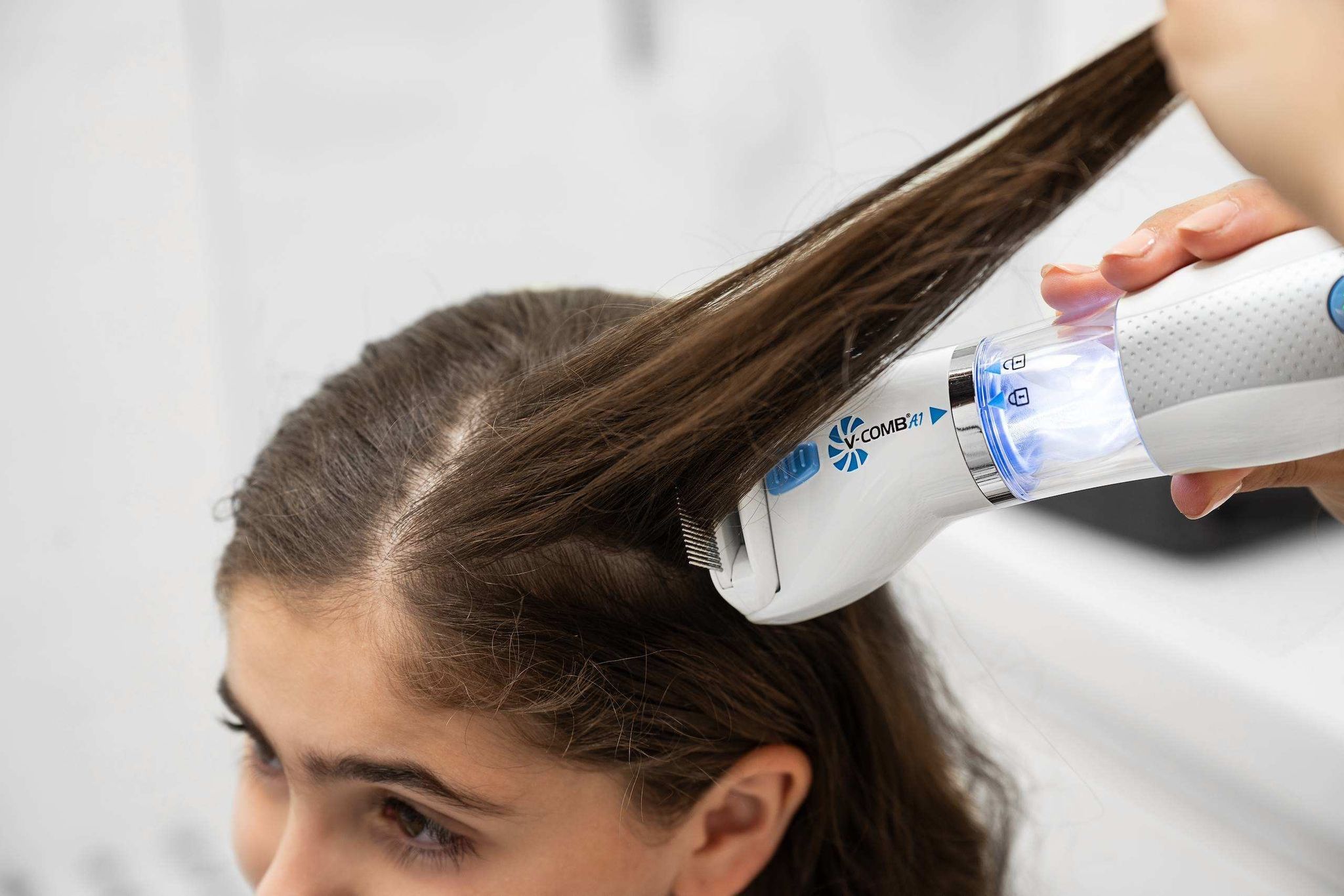 Elektrischer Läusekamm mit blauem und weißem Gehäuse, der auf dem Haar eines Kindes verwendet wird.