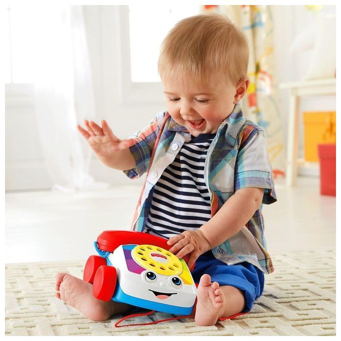 Ein Kleinkind sitzt mit einem Spielzeug-Telefon. Das Telefon hat rote Räder, einen roten Hörer und eine gelbe Wählscheibe.