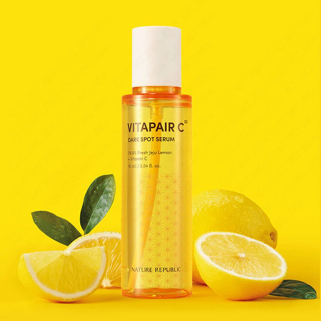 Gelbes Serumfläschchen mit weißem Deckel, umgeben von Zitronen und Blättern. Beschriftung: VITAPAIR C, NATURE REPUBLIC.