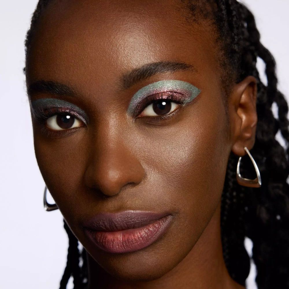 Nahaufnahme einer Frau mit Make-up. Blaue und rosa Lidschatten. Dunkle Haut. Silberne Ohrringe.