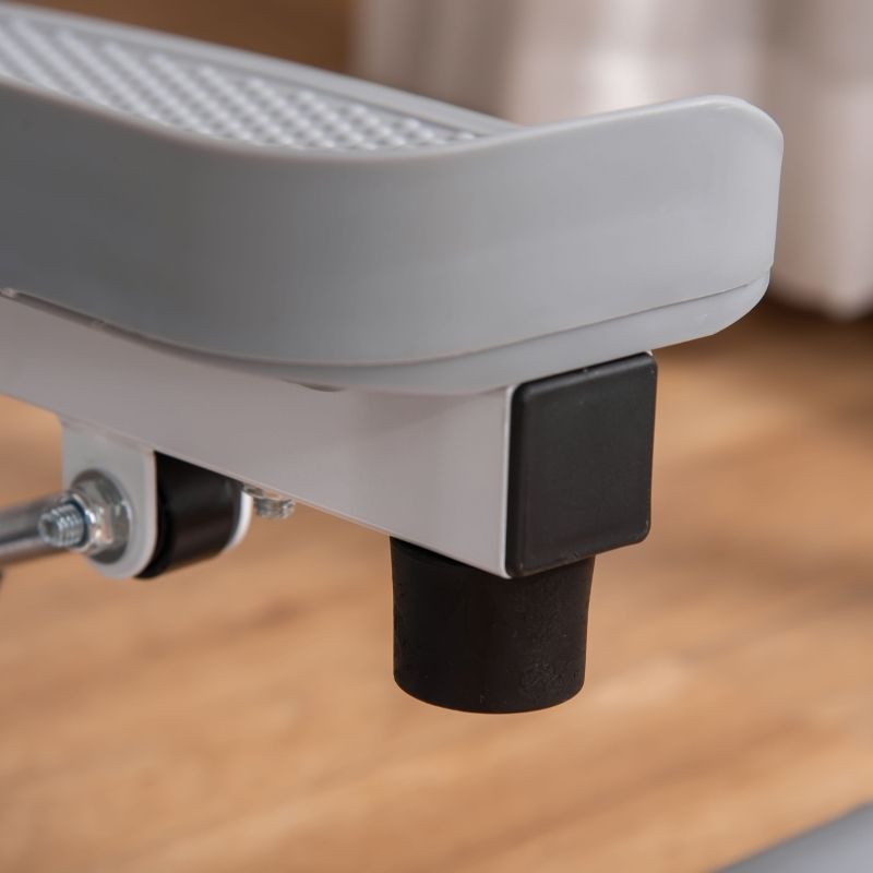 Grauer Stepper-Fuß mit schwarzem Gummifuß. Graue Trittfläche. Weißes Metallgestell. Holzfußboden.