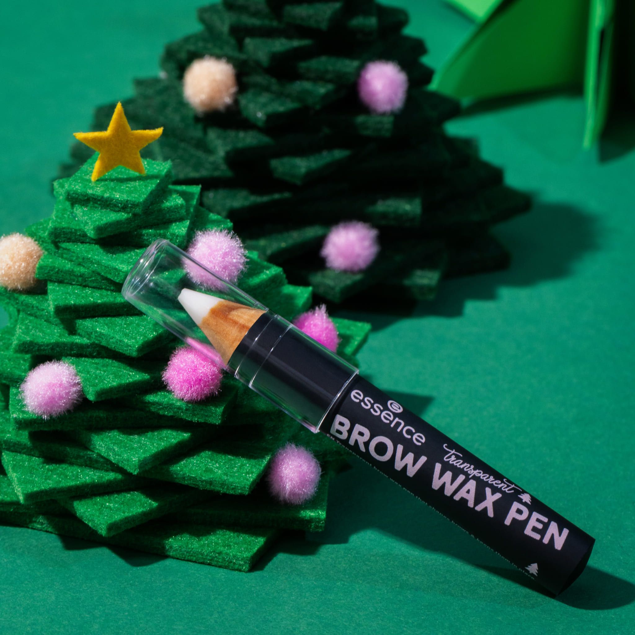 Brauenstift mit transparentem Wachs. Aufschrift « Brow Wax Pen ». Steht vor grünen Tannenbäumen. Dekoration.
