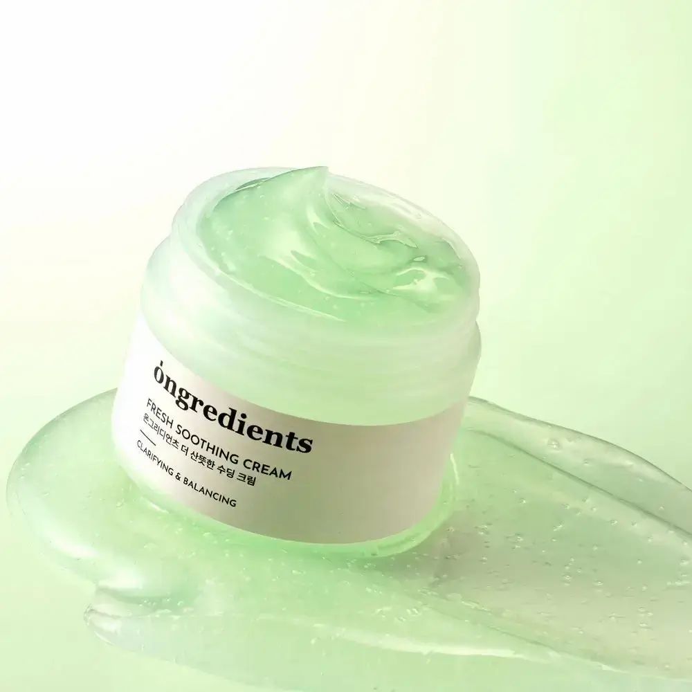 Offenes Creme-Glas mit grüner Creme. Aufschrift: ONGREDIENTS, FRESH SOOTHING CREAM, koreanischer Text, CLARIFYING & BALANCING. Creme auf Untergrund verteilt.