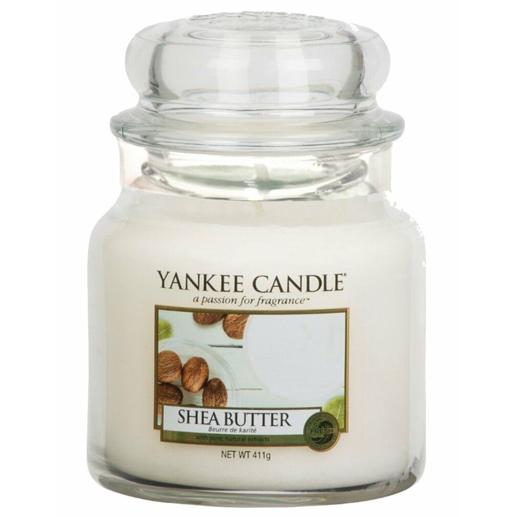 Yankee Candle Shea Butter Duftkerze. Glasbehälter mit Deckel. Etikett mit Produktname und Abbildung von Sheanüssen. Nettogewicht 411g.