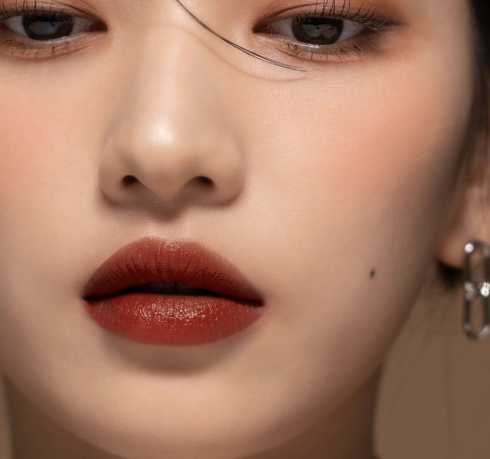 Nahaufnahme von Gesicht mit Lippen. Brauner Lipgloss. Augenbrauen, Augen, Haut. Ohrring.