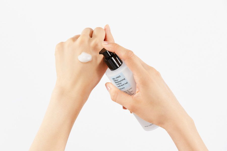 Hände halten eine Flasche und verteilen Lotion. Weiße Lotion auf der Hand. Flasche mit schwarzem Pumpverschluss.