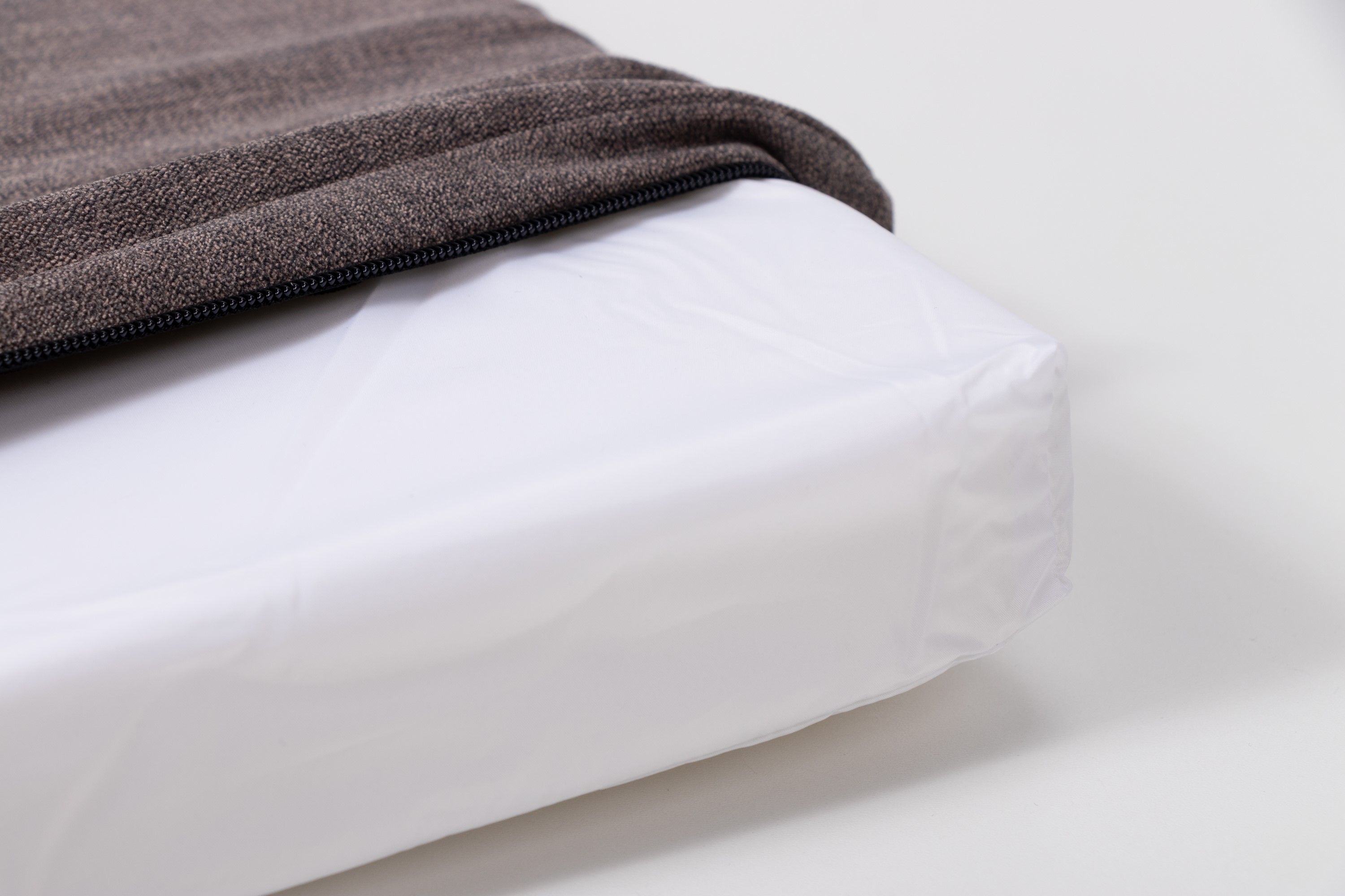 Grauer Matratzenbezug mit Reißverschluss, teilweise geöffnet. Darunter eine weiße, verpackte Matratze.