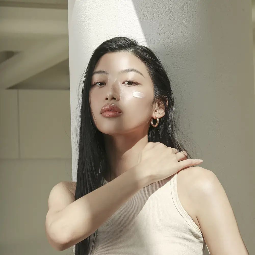 Frau mit langen, dunklen Haaren und Ohrringen. Creme auf der Haut. Natürliches Licht.