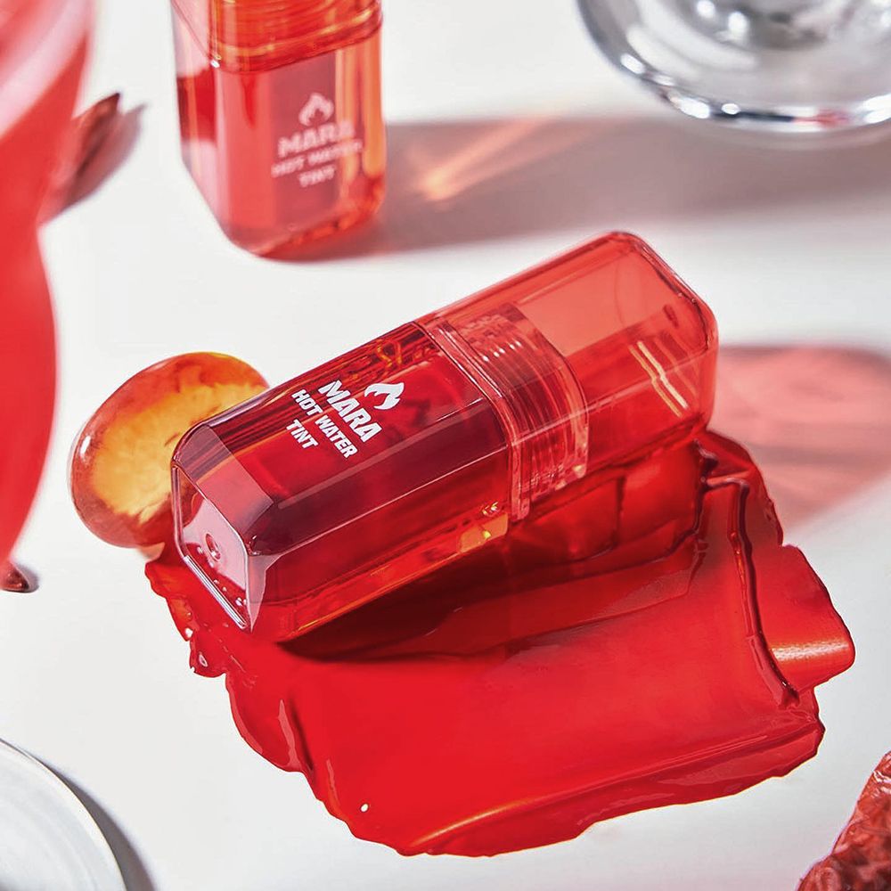 Roter Lip Tint und Farbspritzer auf weißem Untergrund. Produkt und Text.