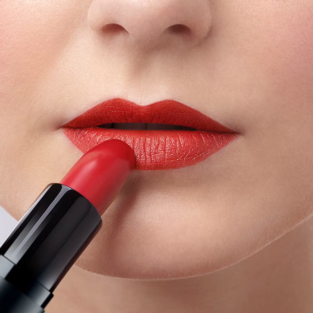 Nahaufnahme von Lippen, die mit rotem Lippenstift bemalt werden. Schwarzer Lippenstift-Halter sichtbar.